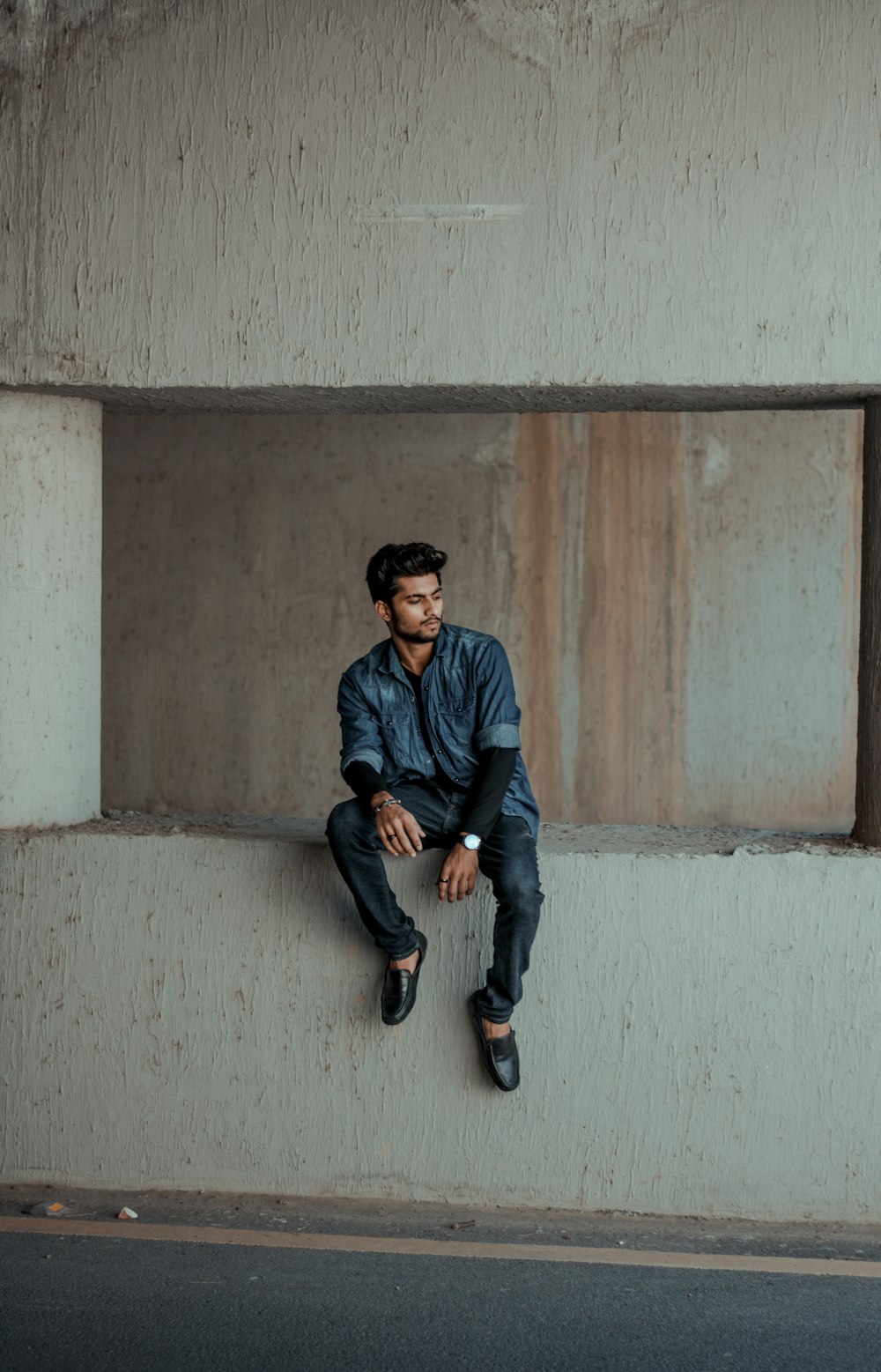 man in blue dress shirt and black pants sitting on white concrete wall