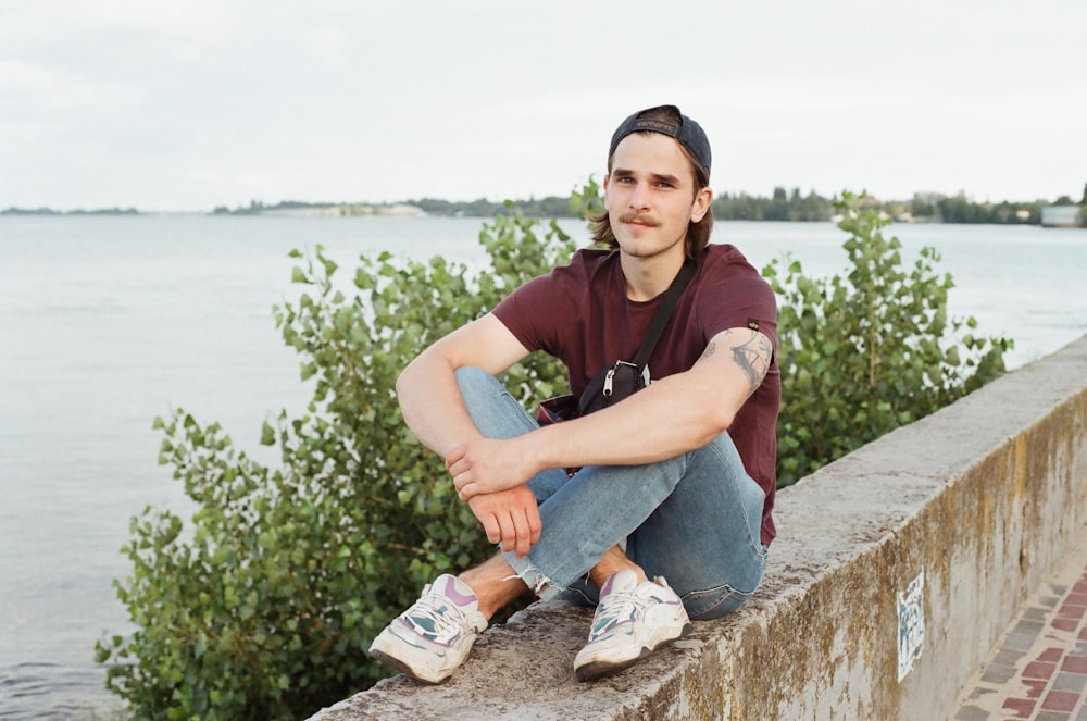 man in maroon polo shirt and blue denim jeans sitting on concrete bench