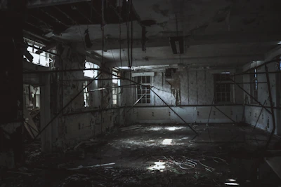 A shadowy corridor inside a vacant building with scattered debris and light filtering through broken windows.