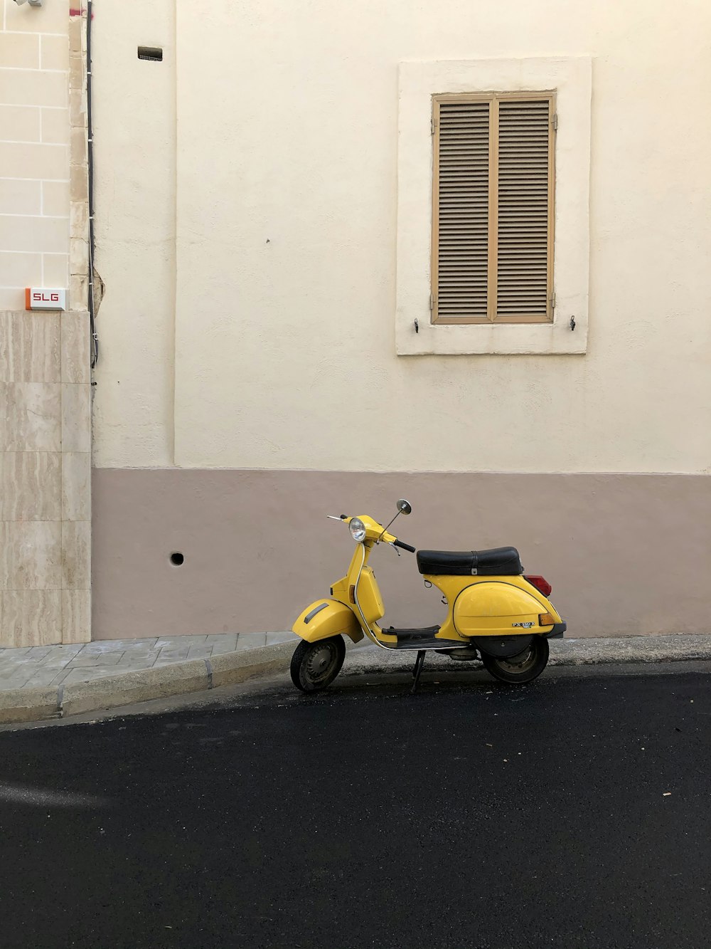 日中、白いコンクリートの建物の脇に駐車された黄色と黒のモータースクーター
