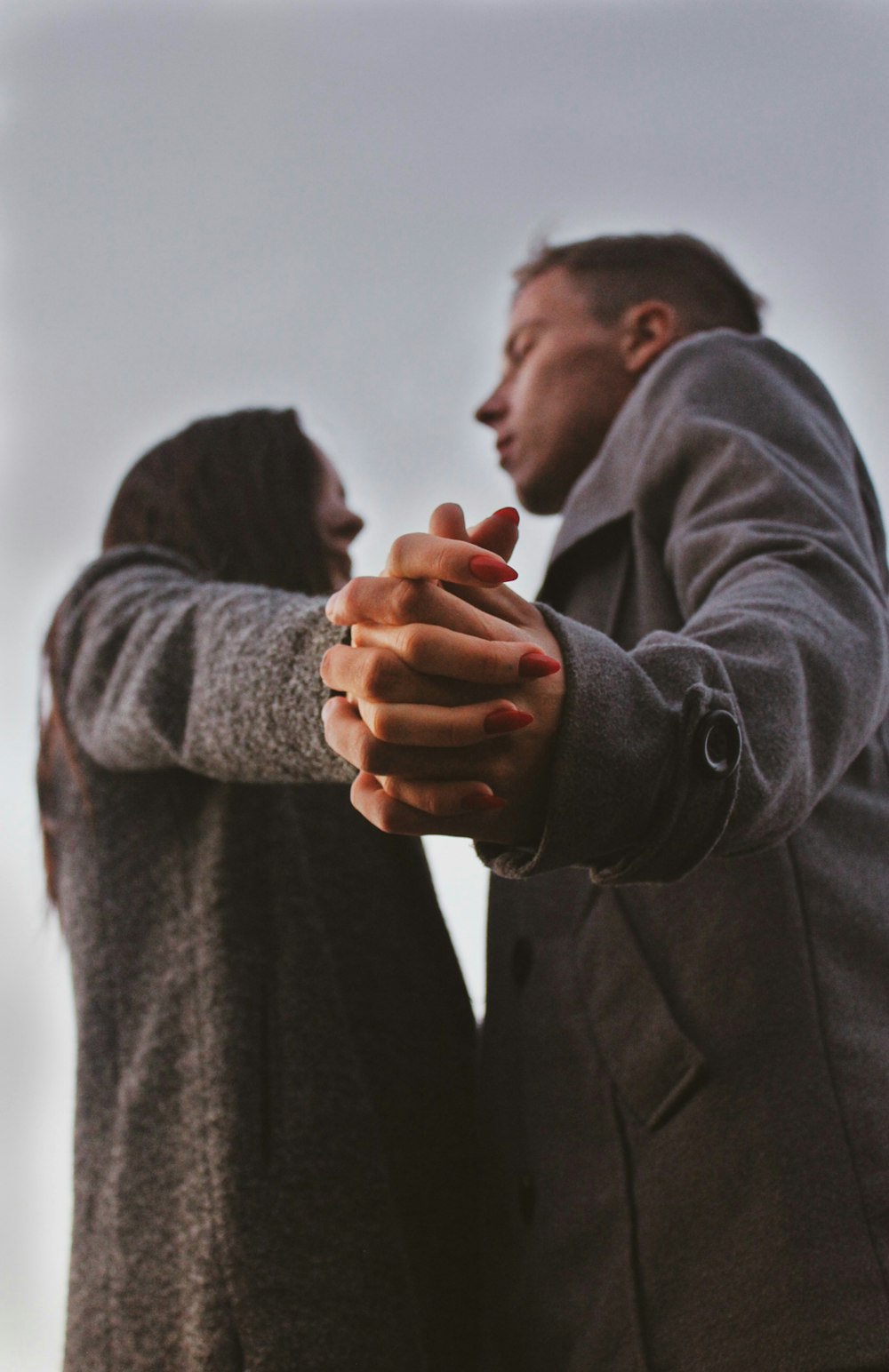man in black coat holding hands of woman in gray sweater