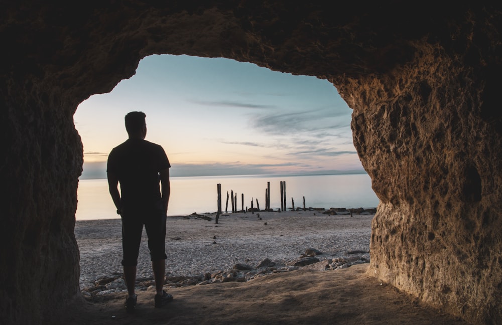 Silhouette eines Mannes, der während des Sonnenuntergangs am Strandufer steht