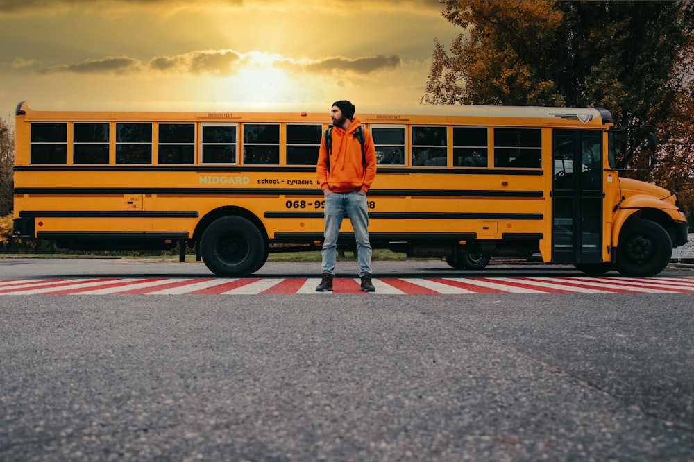 man in blue jacket standing beside yellow school bus during daytime