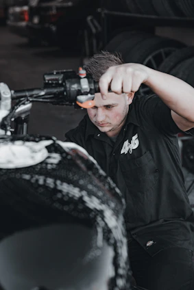 A skilled technician repairing a motorcycle tire on the roadside with a sleek, black and blue van of ÁgilPneu in the background.