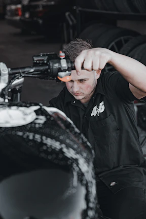A professional mechanic performing a tire change on a motorcycle, surrounded by red, black, and gray workshop elements