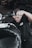 A person wearing a black shirt is actively working on a motorcycle, focusing on a task with determination. The background contains tires stacked in a garage environment.