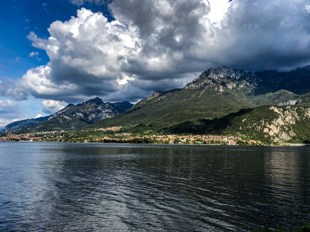 green and white mountain beside body of water under white clouds and blue sky during daytime