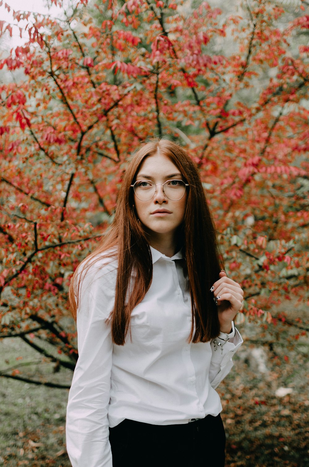 woman in white long sleeve shirt standing near brown leaves tree during daytime