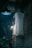 A ghostly figure hangs from the ceiling in a dimly lit space with brick walls. The figure appears to be a doll with a white sheet covering it and is positioned next to a hanging light fixture. Below it, a mannequin leg with a painted red toenail dangles. There is a potted plant partially visible at the bottom left corner.