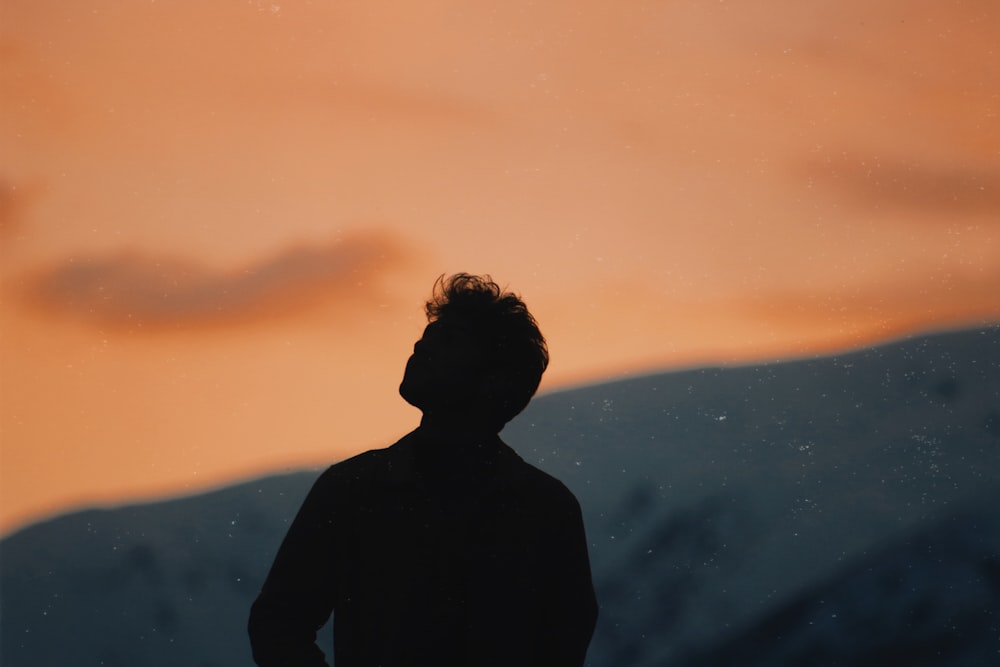 silhouette of man standing on mountain during sunset