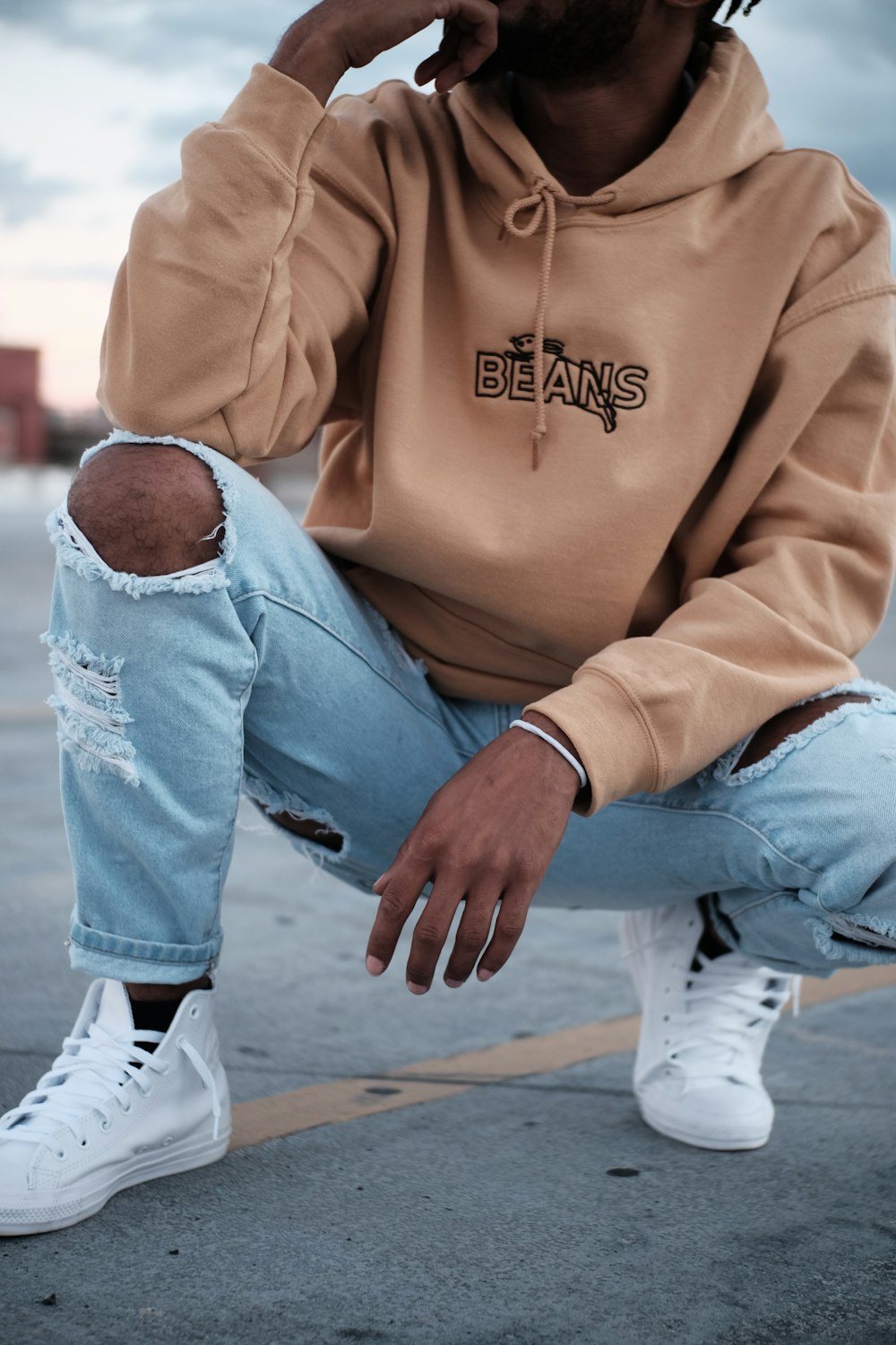 woman in brown hoodie and blue denim jeans sitting on concrete floor during daytime