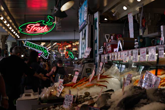 A bustling seafood market with fresh catches displayed on ice under bright lights.