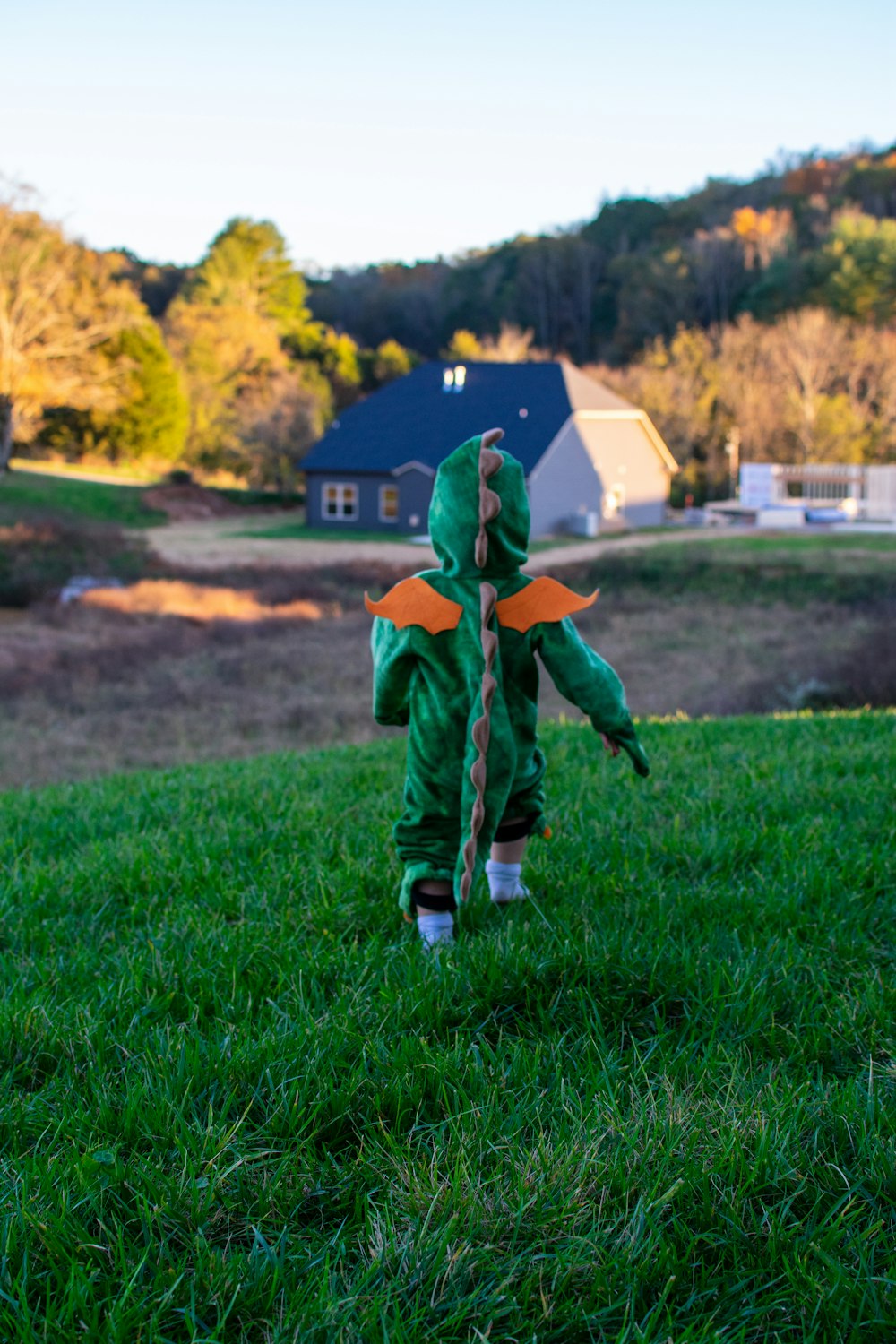낮 동안 푸른 잔디밭을 걷고 있는 녹색과 주황색 재킷을 입은 소년