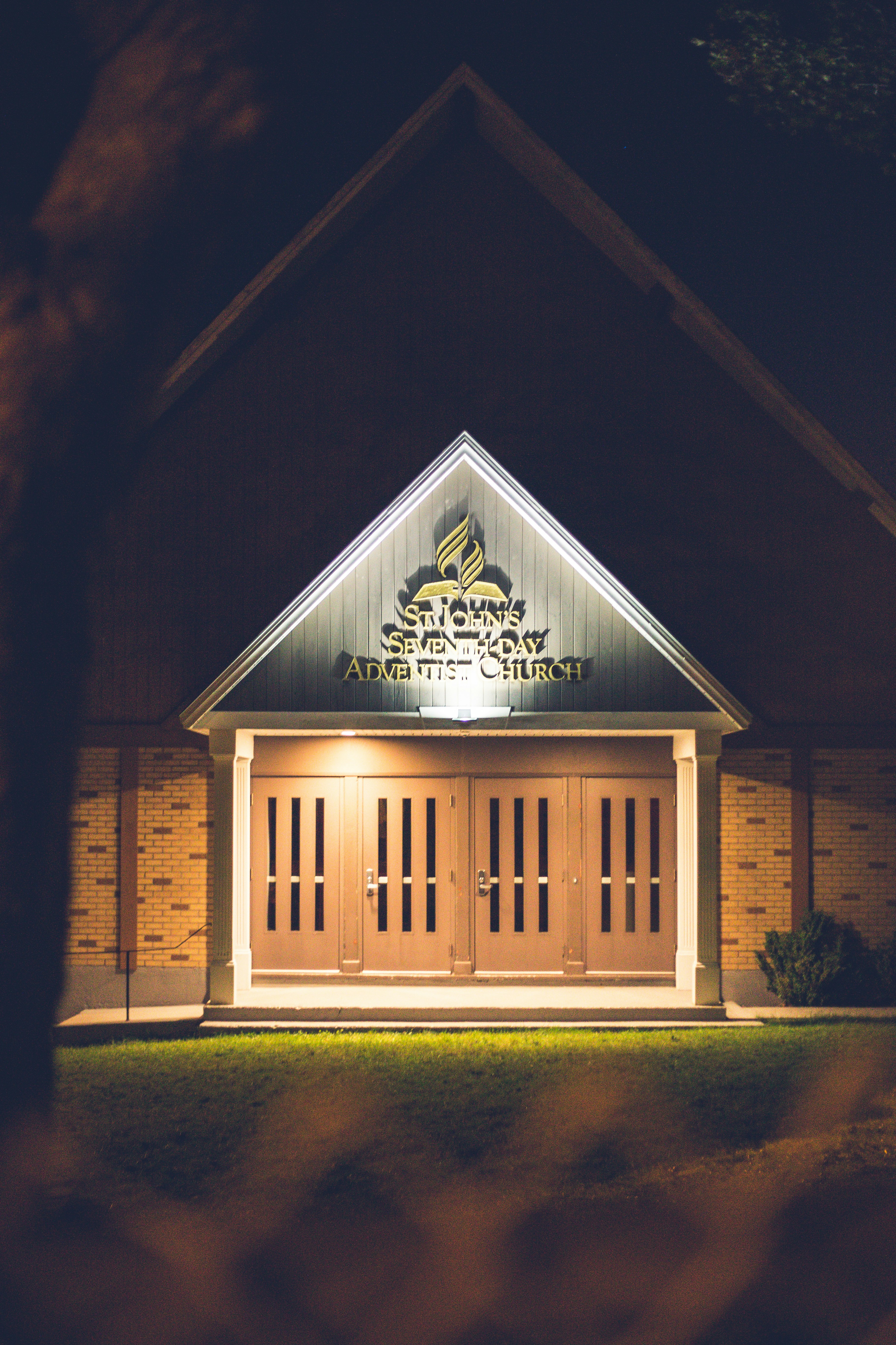Modern church entrance with wooden doors illuminated at night.