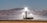 Three tall, industrial-looking solar power towers are located in a desert landscape with mountains in the background. The towers are brightly illuminated at the top, likely from concentrated sunlight. Surrounding the towers are arrays of mirrors used to direct sunlight towards the towers.