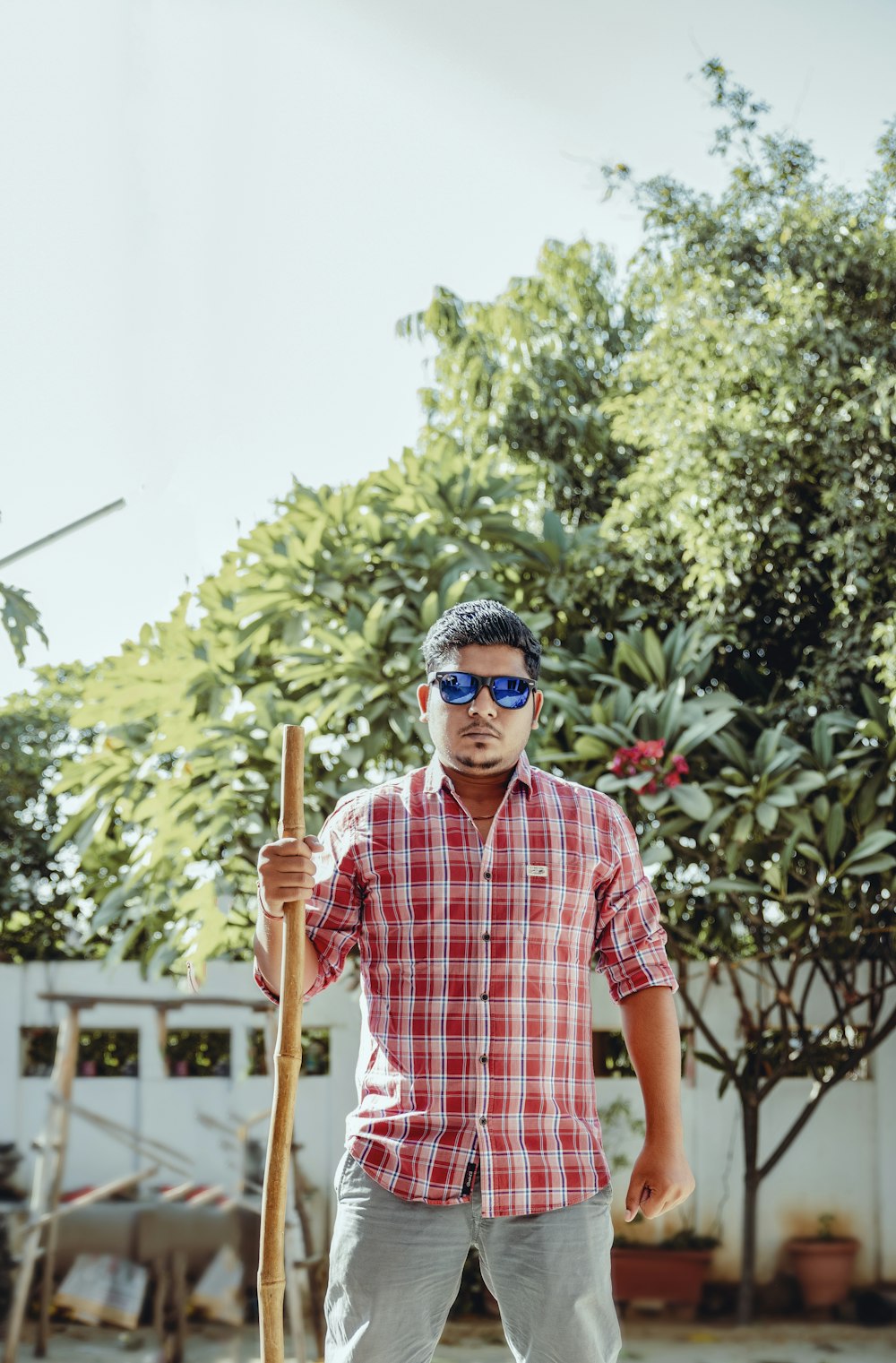 man in red and white plaid button up t-shirt holding brown wooden stick