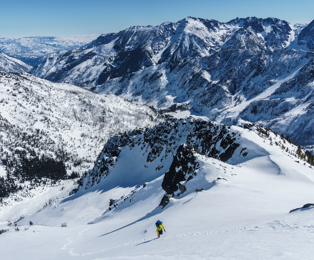 person in blue jacket and yellow pants standing on snow covered mountain during daytime