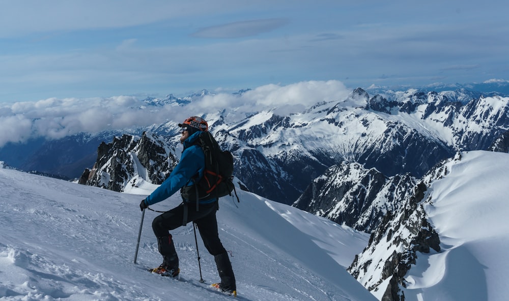 Hombre en chaqueta azul y pantalones negros montando hojas de esquí en la montaña cubierta de nieve durante el día