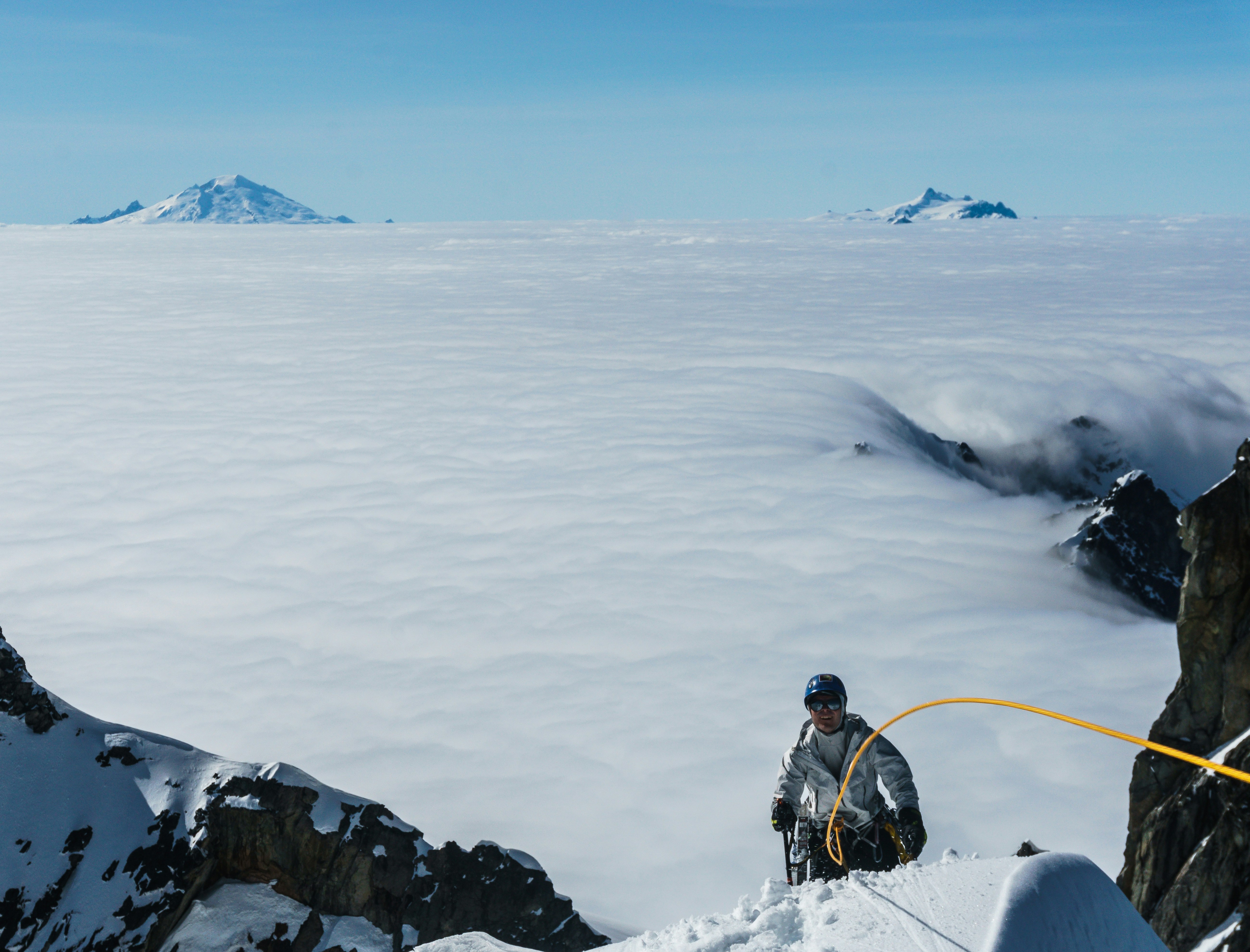 man in black jacket sitting on rock formation covered with snow during daytime, Climbing above the clouds in the North Cascades of Washington US