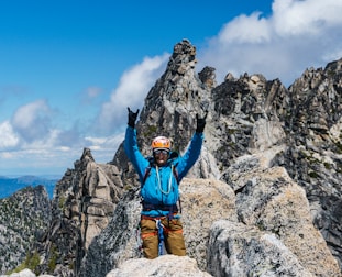 man in blue jacket and brown pants sitting on rock formation during daytime
