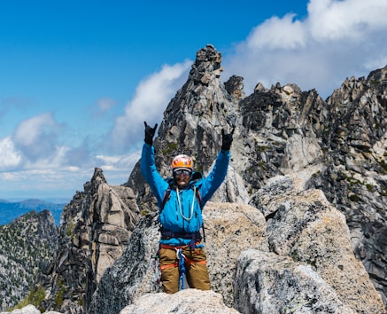man in blue jacket and brown pants sitting on rock formation during daytime