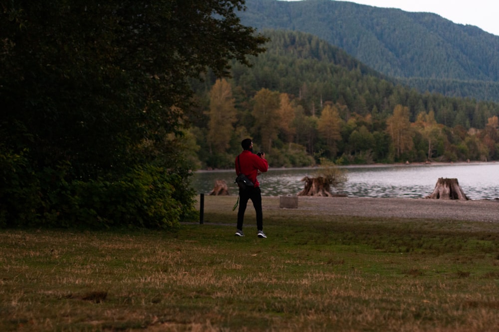 person in red jacket standing on green grass field near body of water during daytime