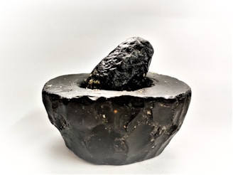 Artisanal mortar and pestle set on a basalt stone surface with scattered peppercorns.