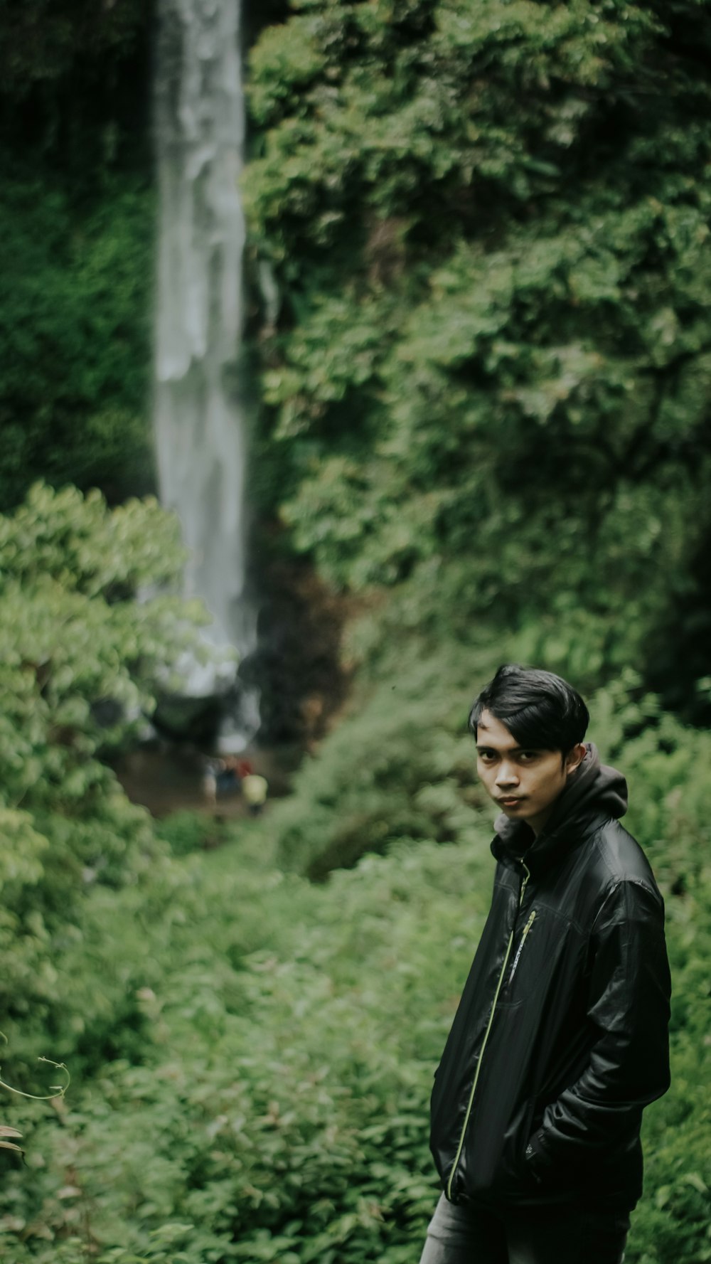 man in black leather jacket standing near green trees during daytime