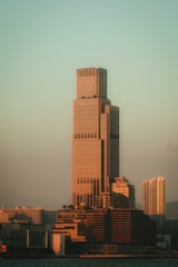 A modern building rising over a city skyline under a warm sunset.