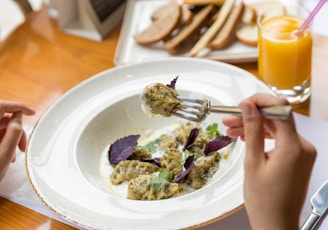 person holding stainless steel fork on white ceramic plate