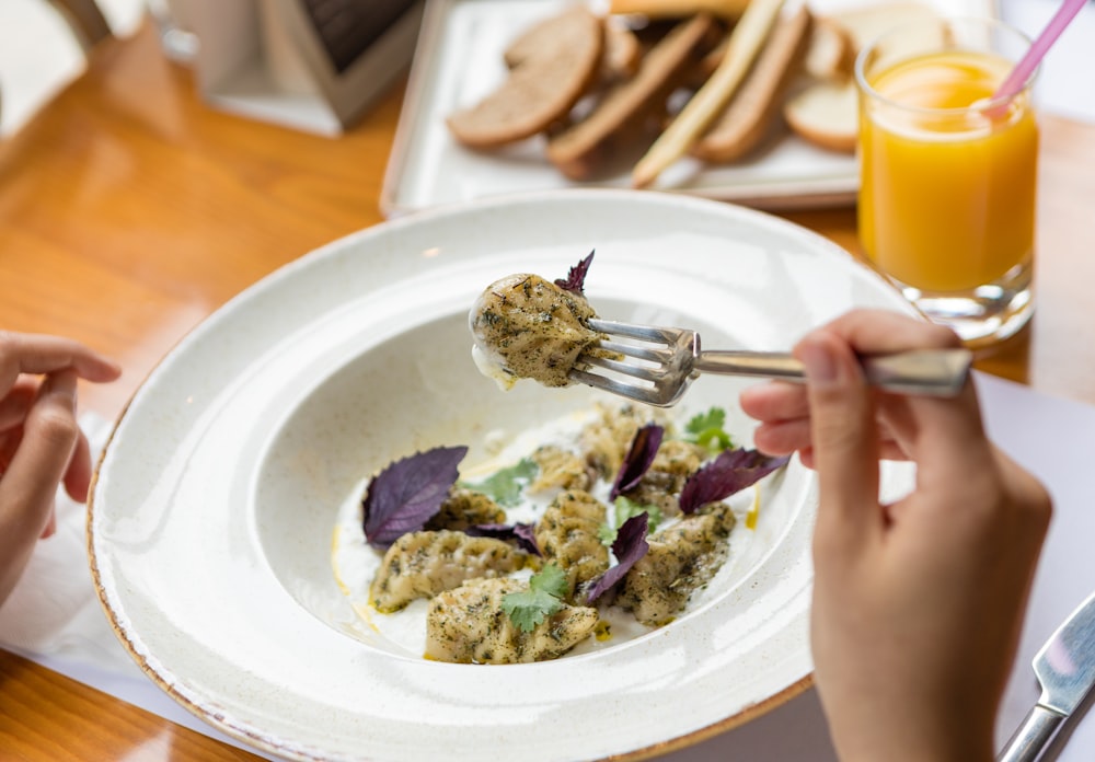 person holding stainless steel fork on white ceramic plate