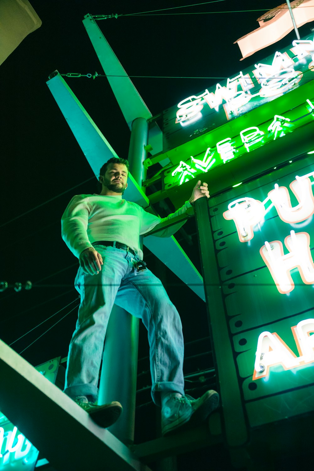 man in green t-shirt and blue denim jeans sitting on green metal bar