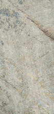 A close-up view of a textured stone surface, displaying natural patterns and veins across its surface. The stone has a subtle mix of neutral tones with some darker patches and lighter streaks.