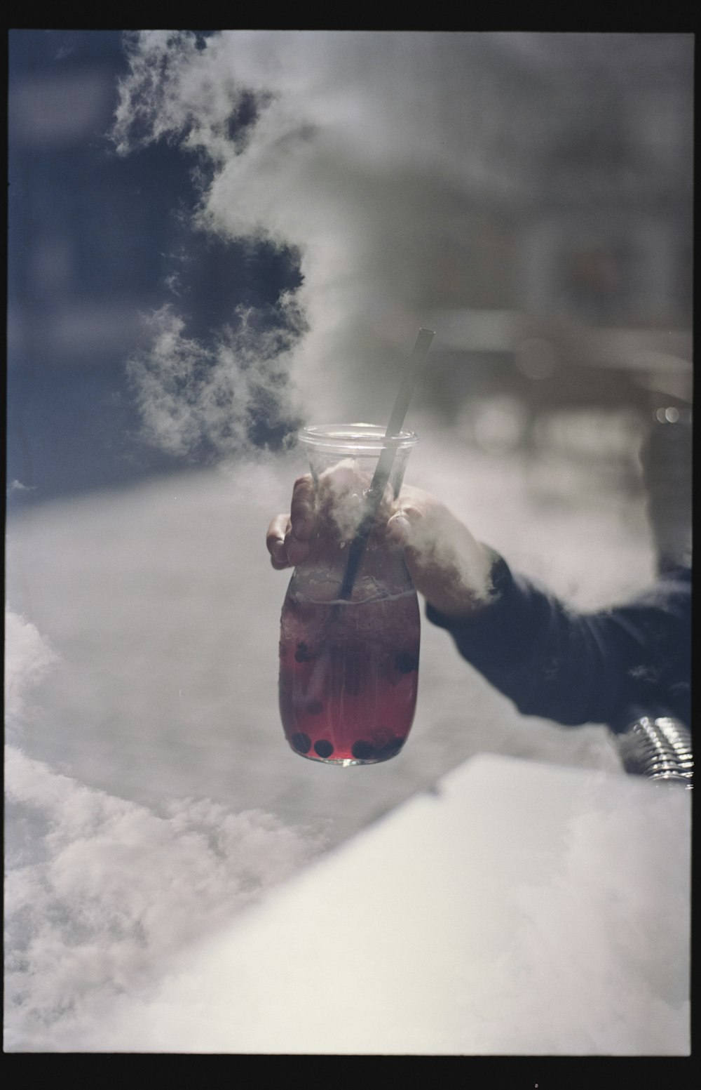 person in black jacket holding clear plastic cup with red liquid