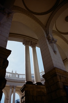 Elegant architectural structure featuring tall, white columns and stone arches, with a circular balcony providing an open view to the sky. The design showcases classical elements and intricate details at the column tops.