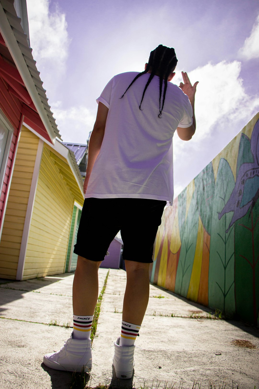 man in white t-shirt and black shorts standing beside wall with graffiti during daytime