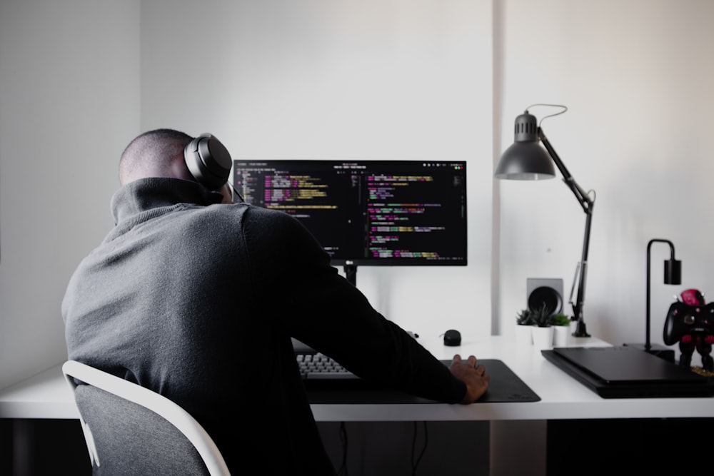 Mann im schwarzen Langarmhemd sitzt auf einem Stuhl vor dem Computer