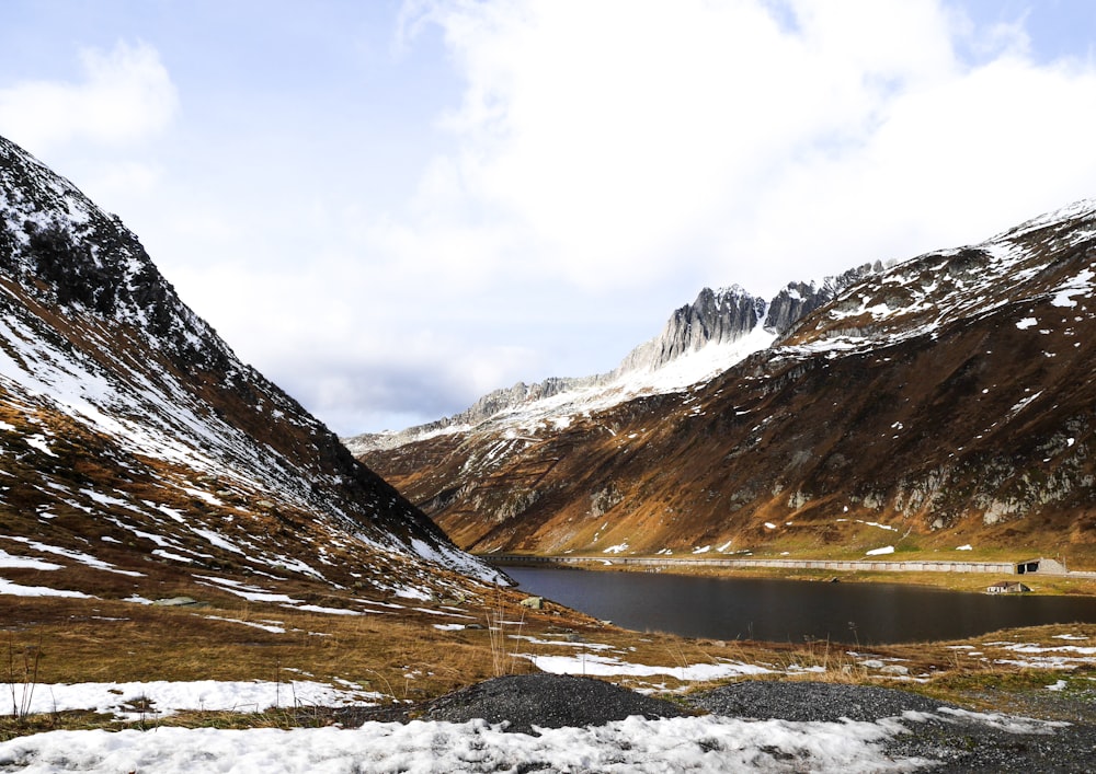 brown and white mountains near lake under white clouds during daytime