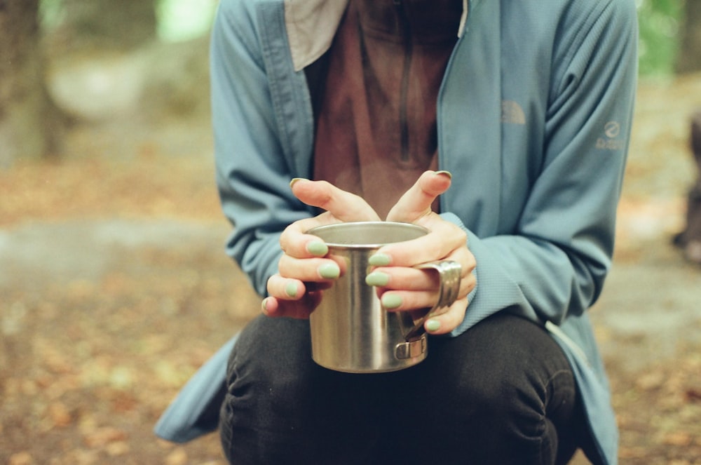 man in blue jacket holding stainless steel cup