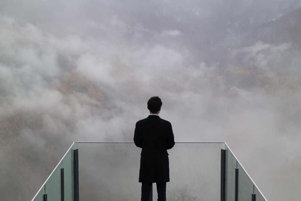 man in black coat standing on top of building under cloudy sky