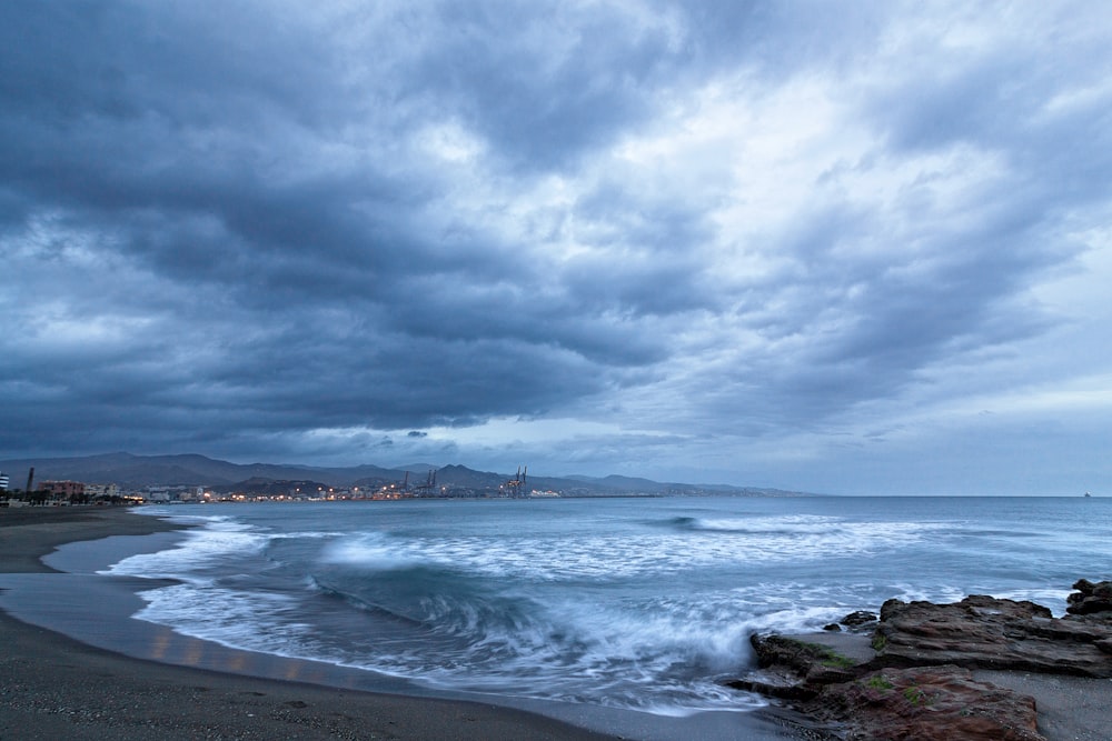 sea waves crashing on shore under cloudy sky during daytime