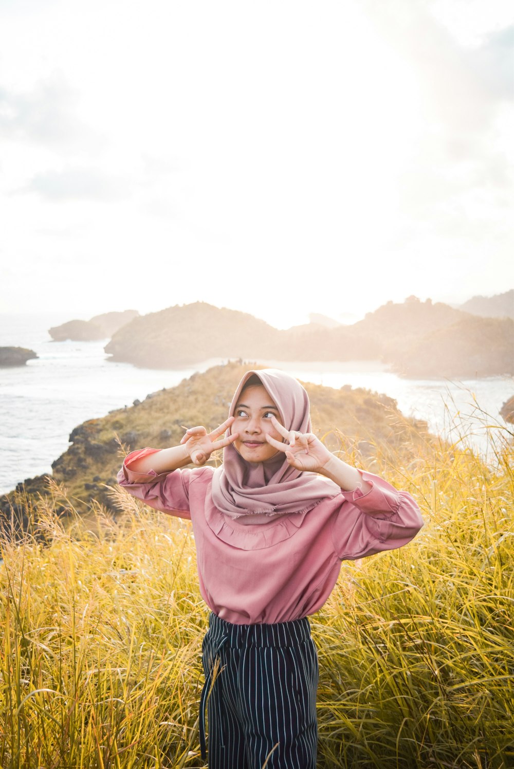 woman in pink hijab standing on green grass field near body of water during daytime