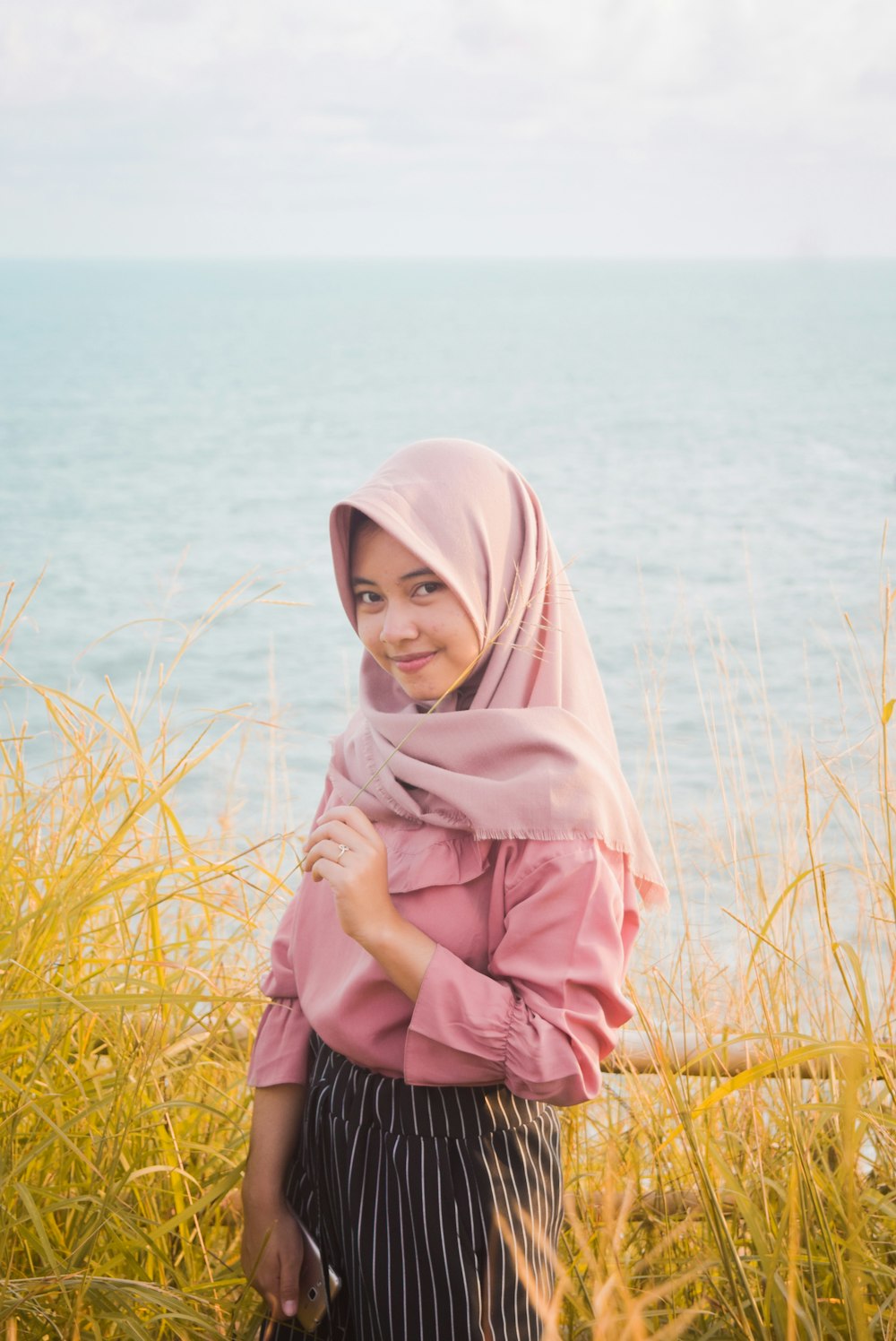 woman in pink hijab standing on green grass field near body of water during daytime