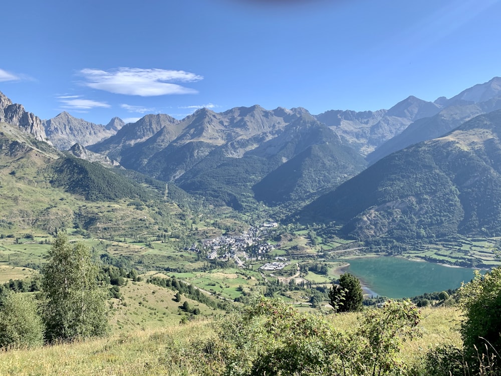 campo de hierba verde cerca del lago y las montañas bajo el cielo azul durante el día