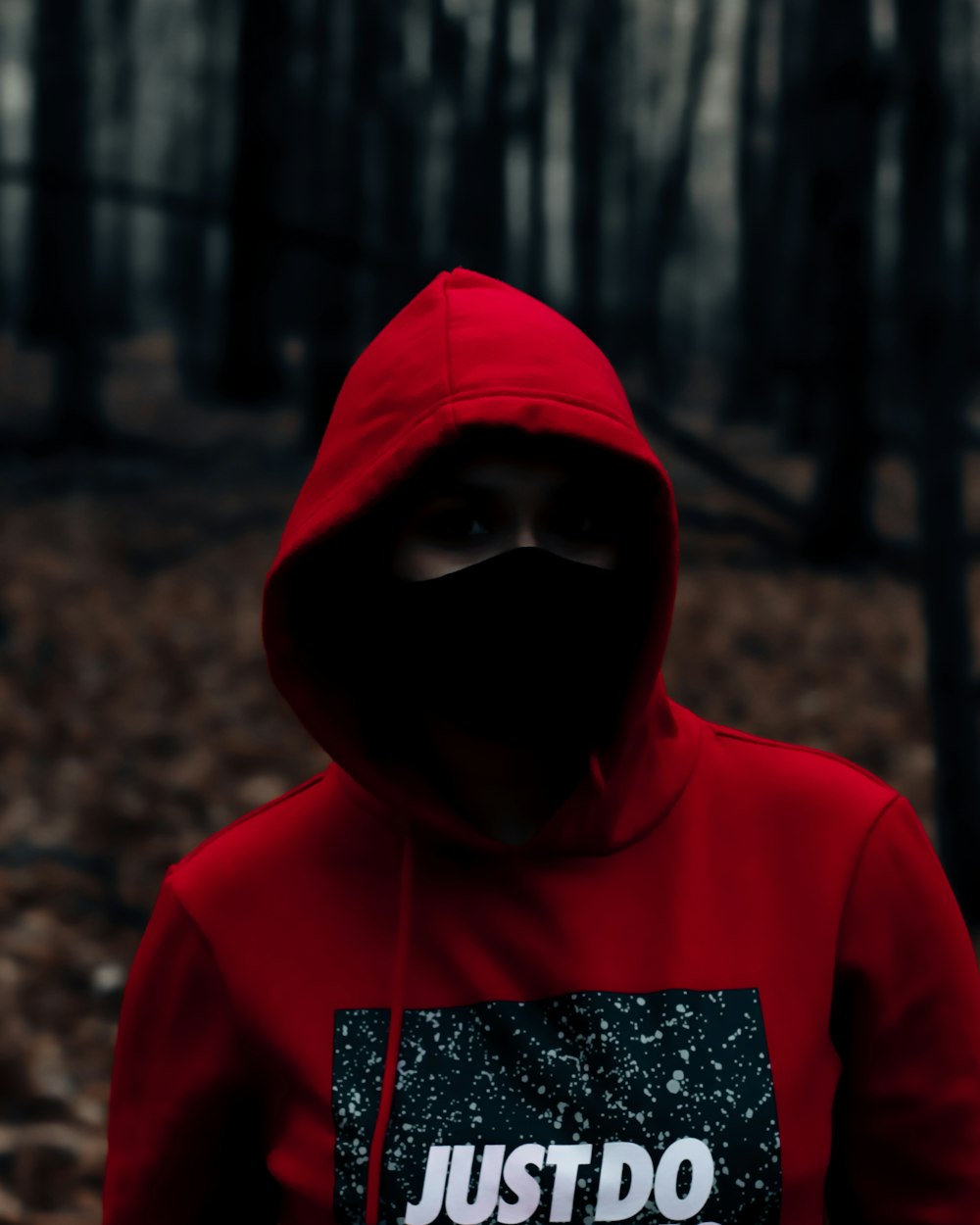 man in red hoodie standing near brown trees during daytime