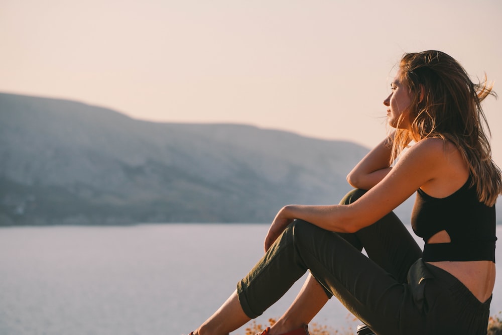 woman in black tank top and black pants sitting on brown wooden bench during daytime