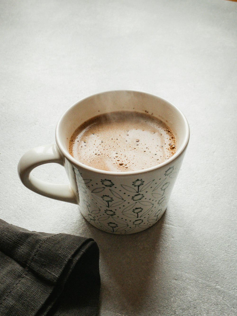 white and black floral ceramic mug with brown liquid