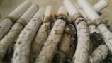 A collection of partially burned cigarettes with white filters and ash-streaked bodies, arranged close together. The brand name is visible near the filters.