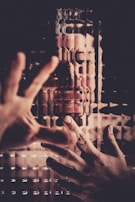 A person is seen through a textured, distorted surface with hands pressed against it. The image gives an impression of struggle or confinement, with the figure's facial expression suggesting distress or frustration.