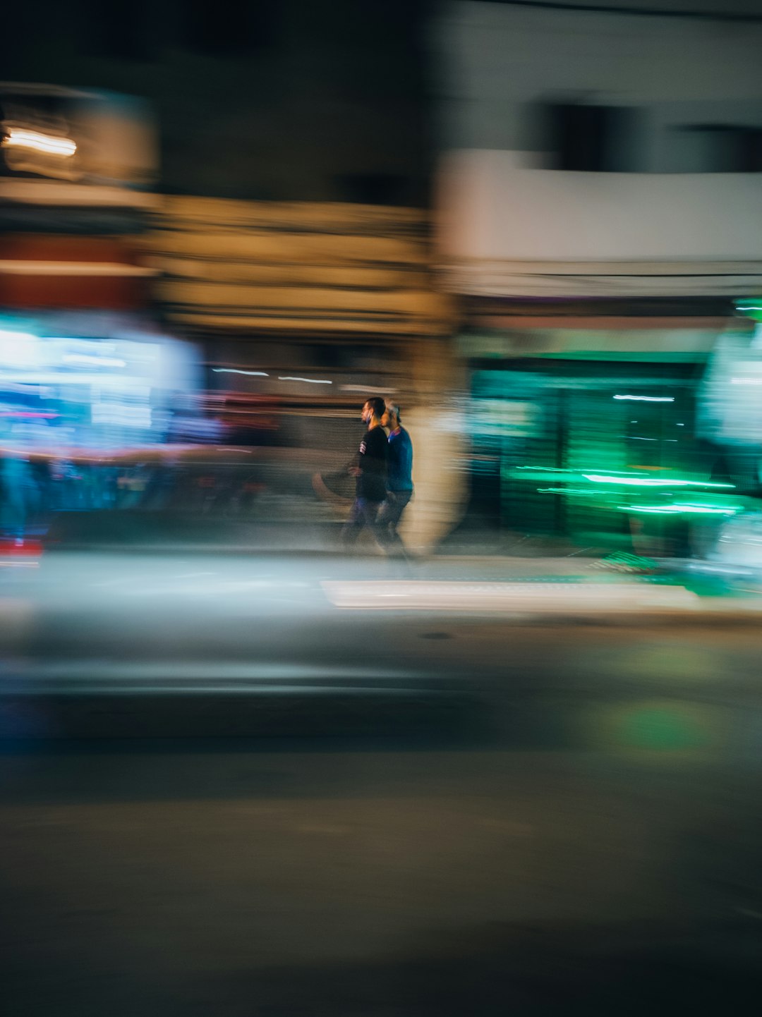 man in black jacket and blue denim jeans walking on street during night time